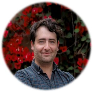 Man smiling in front of red flowers.